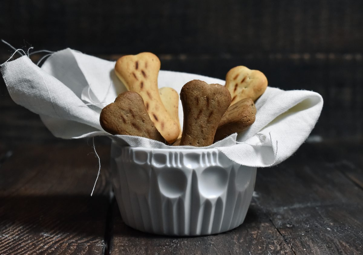 Bone-shaped baked dog treats in a white ceramic bowl on a dark wooden table